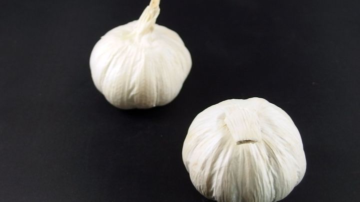 Zwei Knoblauchknollen liegen auf einem schwarzen Untergrund, bereit zur Verwendung in verschiedenen Gerichten.