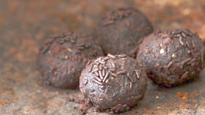 Schokoladenkugeln liegen auf einer rustikalen Oberfl&auml;che und zeigen ihre gl&auml;nzende, dunkle Beschichtung mit feinen Dekoren.