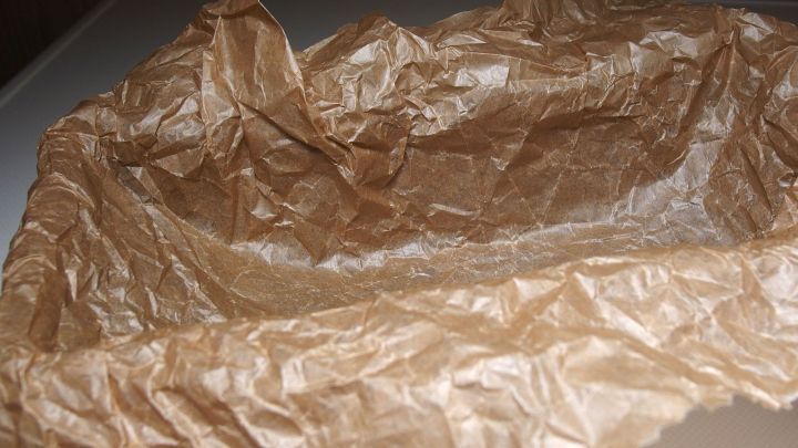 Ein zerknittertes St&uuml;ck Backpapier liegt auf einer glatten Oberfl&auml;che und ist bereit zum Auslegen f&uuml;r das Backen.