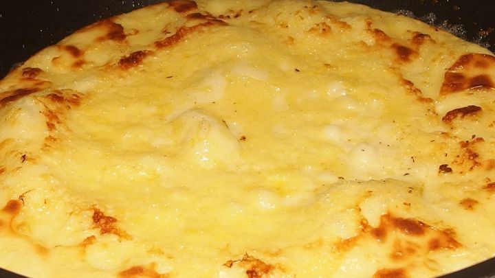 Ein rundlicher, goldbraun gebratener Pfannkuchen liegt in einer schwarzen Pfanne und ist gleich fertig zum Servieren.