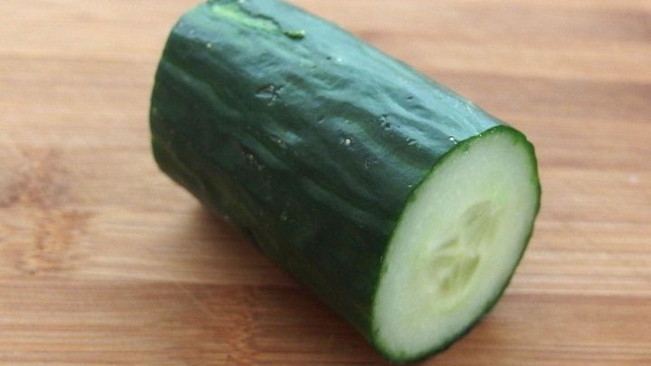 Eine gr&uuml;ne Salatgurke liegt auf einem Holzbrett, halbiert und zeigt das frische, saftige Innere.