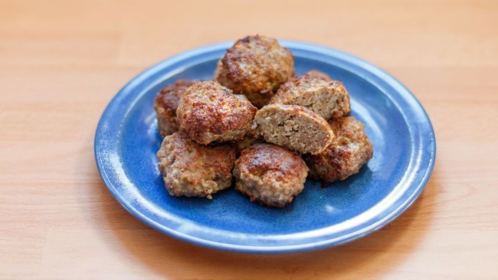 Auf einem blauen Teller liegen mehrere goldbraun gebratene Frikadellen. Eine ist zur H&auml;lfte aufgeschnitten und zeigt ihr leicht fluffiges Innere.