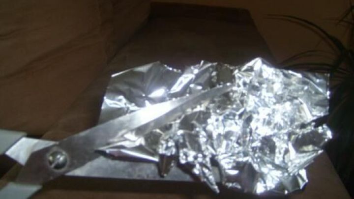 Eine Schere schneidet durch zerknitterte Alufolie auf einer Couch, was einem praktischen Lebenshack zur Sch&auml;rfung dient.