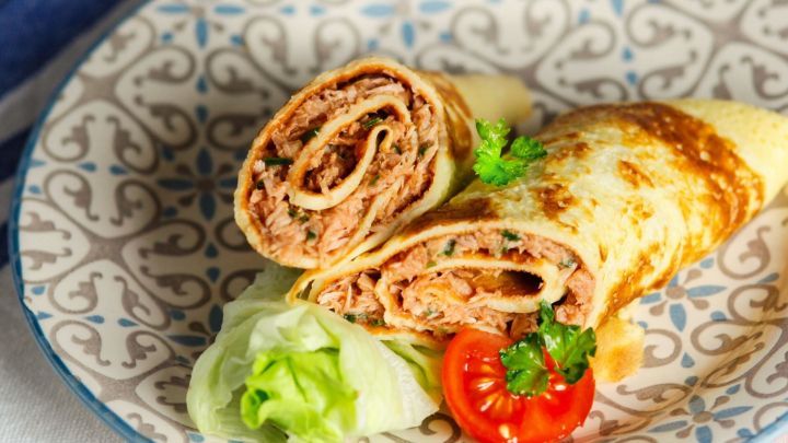 Eierpfannkuchen mit Thunfisch liegen auf einem dekorativen Teller, umgeben von Tomate und Salat.