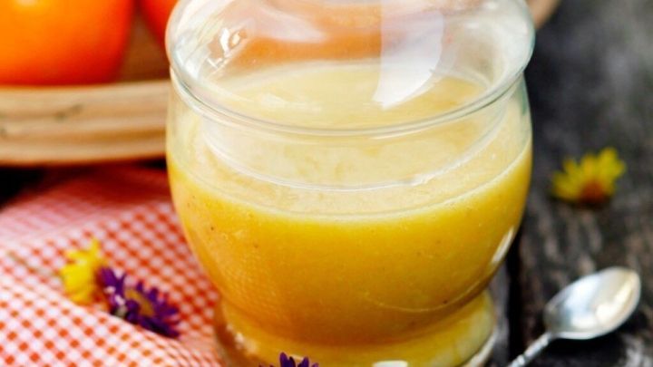 Ein Glas Orangenmarmelade steht auf einem rustikalen Holztisch, umgeben von frischen Orangen und bunten Blumen.