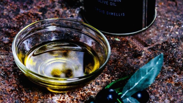 Eine Schale mit Oliven&ouml;l steht auf einem rustikalen Tisch, umgeben von Oliven und einem Oliven&ouml;lbeh&auml;lter, passend zum Thema.