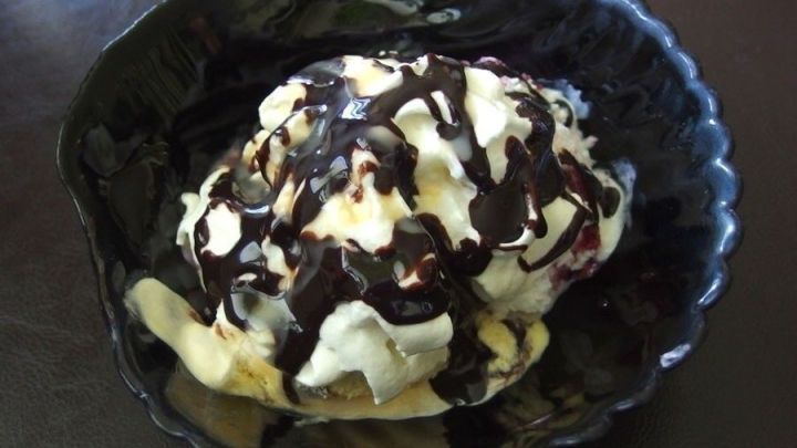 Ein dunkler Schalenbecher enth&auml;lt eine kalte Eisschicht, die mit Schokoladensauce und Sahne &uuml;berzogen ist.