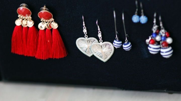 Ohrringe sind an einer schwarzen Unterlage angeordnet, einige sind rot, andere in Herzform, w&auml;hrend weitere farbenfroh beklagt sind.