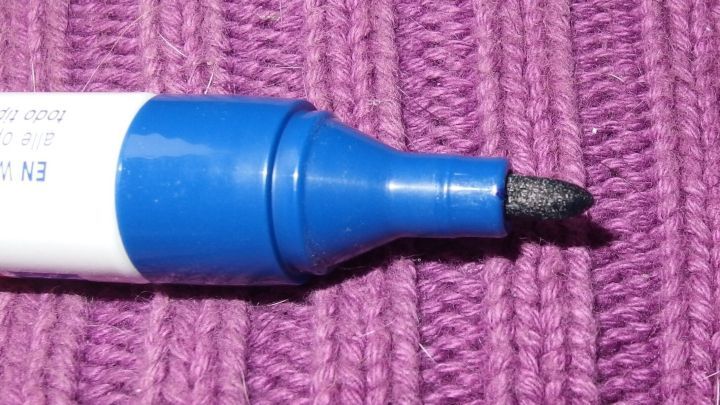 Ein schwarzer Permanentmarker liegt auf einem lila gestrickten Stoff, bereit zum Zeichnen oder Schreiben.