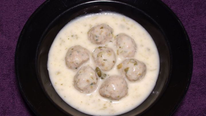 Eine Sch&uuml;ssel mit wei&szlig;en (Creme-)Suppen enth&auml;lt mehrere runde Fleischb&auml;llchen und steht auf einem lila Hintergrund.