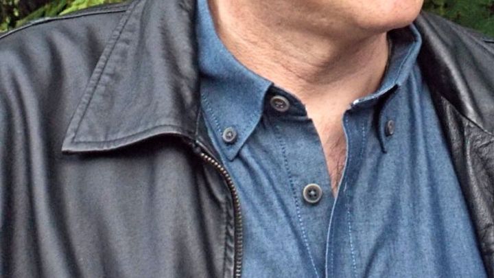 Ein Mann tr&auml;gt eine Nappalederjacke &uuml;ber einem blauen Hemd, umgeben von gr&uuml;nem Laub im Freien.