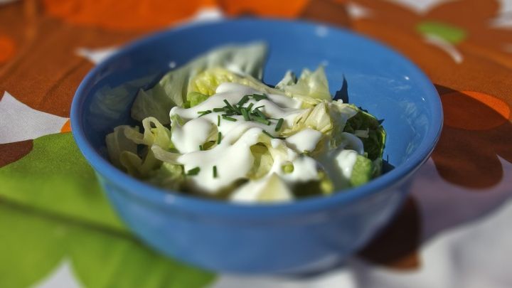 Ein blauer Sch&uuml;ssel enth&auml;lt knackigen Eisbergsalat mit einer s&uuml;&szlig;en Salatsauce, platziert auf einem bunten Tisch.