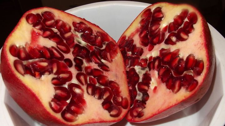 Eine halbierte Granatapfelh&auml;lfte zeigt saftige, rote Kerne in einer wei&szlig;en Sch&uuml;ssel, bereit zur Zubereitung.