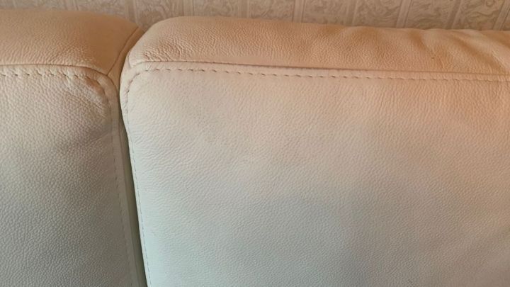 Eine helle Kunstledercouch zeigt Farbflecken an den Kanten, die m&ouml;glicherweise mit Nagellackentferner behandelt werden sollen.