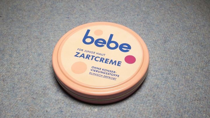 Eine runde Lippencreme-Dose mit der Aufschrift "bebe ZARTCREME" liegt auf einer grauen Oberfl&auml;che.