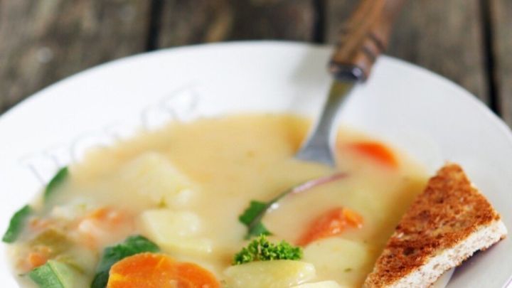 Eine cremige Kartoffelsuppe wird in einer wei&szlig;en Sch&uuml;ssel serviert, umgeben von frischem Gem&uuml;se und einem St&uuml;ck Brot.