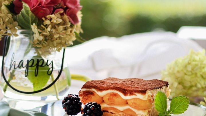 Einschichtiges Tiramisu liegt auf einem Teller, umgeben von Blumen, in einem hellen, nat&uuml;rlichen Ambiente.