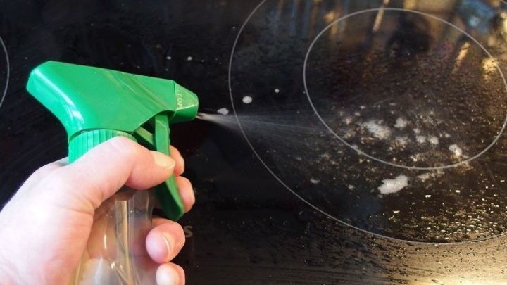 Ein Hand h&auml;lt einen gr&uuml;nen Spr&uuml;hkopf, der Fensterreiniger auf ein sauberes Glaskeramikfeld spr&uuml;ht.