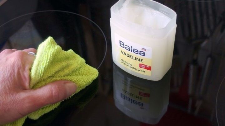 Ein Handtuch reinigt ein gl&auml;nzendes Glaskeramikfeld, w&auml;hrend eine Vaseline-Dose daneben steht.