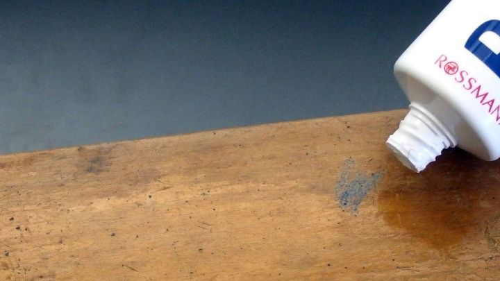 Ein Buntstift wird mit einer Tube Reinigungsmittel von einem Holzbrett entfernt, das eine unebenm&auml;&szlig;ige Oberfl&auml;che zeigt.