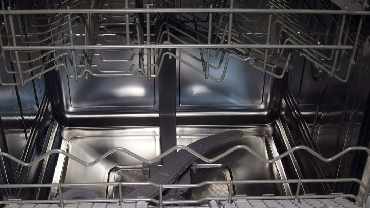 Eine leere Sp&uuml;lmaschine zeigt den Innenraum, der zur Reinigung bereit ist, mit gl&auml;nzenden Metallelementen und Regalen.