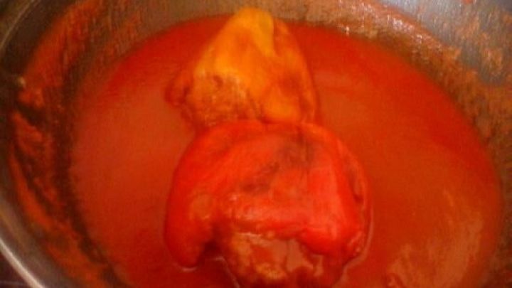 In einer Pfanne schwimmen gef&uuml;llte Paprikaschoten in einer roten So&szlig;e, die k&ouml;chelt und dampft.