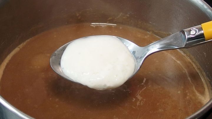 Ein L&ouml;ffel Quark wird in eine kochende Br&uuml;he gegeben, um als kalorienarmer So&szlig;enbinder zu wirken.