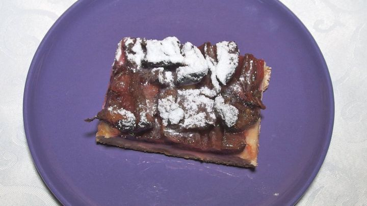 Ein St&uuml;ck Hefeteiggeb&auml;ck liegt auf einem lila Teller, bedeckt mit Schokoladenso&szlig;e und Puderzucker.