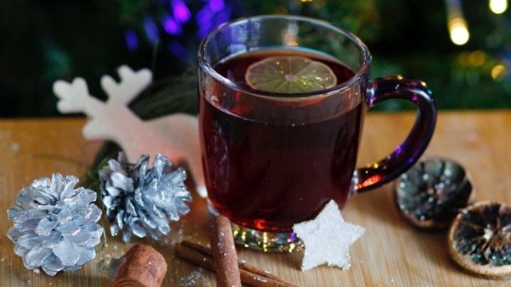 Ein Glas duftender Punsch steht auf einem Holzbrett, umgeben von Zimt, Tannenzapfen und Weihnachtsdekoration.