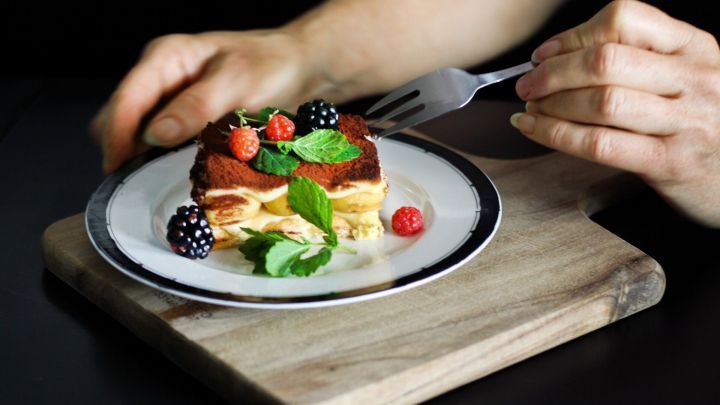 Ein St&uuml;ck kalorienarmes Tiramisu wird auf einem Teller mit frischen Beeren und Minze genossen, bereit zum Essen.
