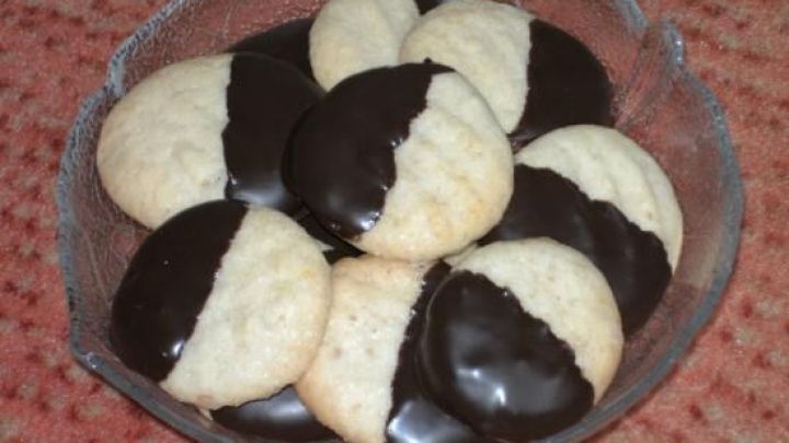 Kleine Ingwerpl&auml;tzchen liegen in einer Sch&uuml;ssel, die H&auml;lfte ist mit Schokolade &uuml;berzogen, umgeben von einem roten Tisch.