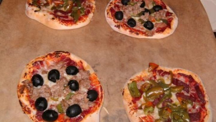 Vier Mini-Pizzen mit Oliven und Paprika auf einem Backblech im Ofen gebacken. Sie verwenden Br&ouml;tchenteig aus der Dose.