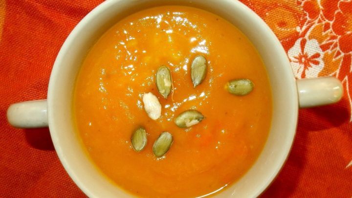 Eine schlichte wei&szlig;e Sch&uuml;ssel enth&auml;lt eine cremige, orangefarbene M&ouml;hren-K&uuml;rbissuppe, dekoriert mit K&uuml;rbiskernen.