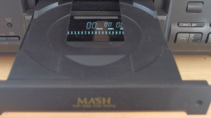 CD-Laufwerk &ouml;ffnet sich, zeigt Display mit "TRACK" und "INDEX" in einem Hifi-Ger&auml;tumfeld. Text: "MASH".