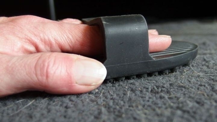 Eine Hand dr&uuml;ckt eine Gummib&uuml;rste &uuml;ber einen Teppich, um Tierhaare zu entfernen. Der Teppich ist grau und strukturiert.