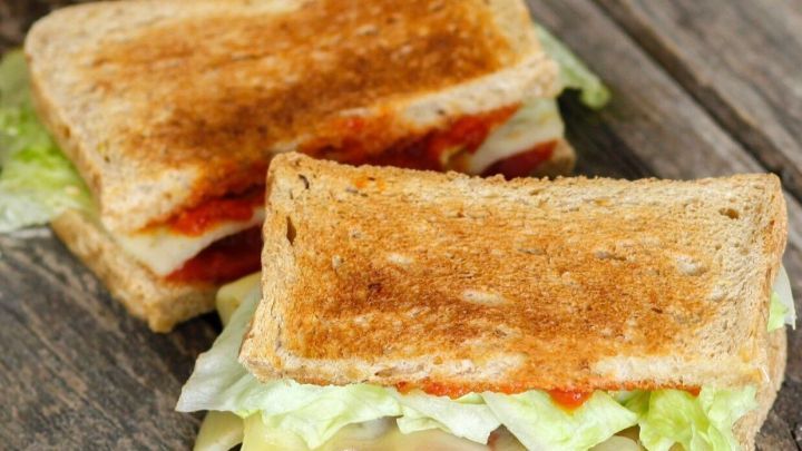 Ein Sandwich aus Toastbrot ist mit Tomatenso&szlig;e und frischem Gem&uuml;se auf einem rustikalen Holztisch angerichtet.
