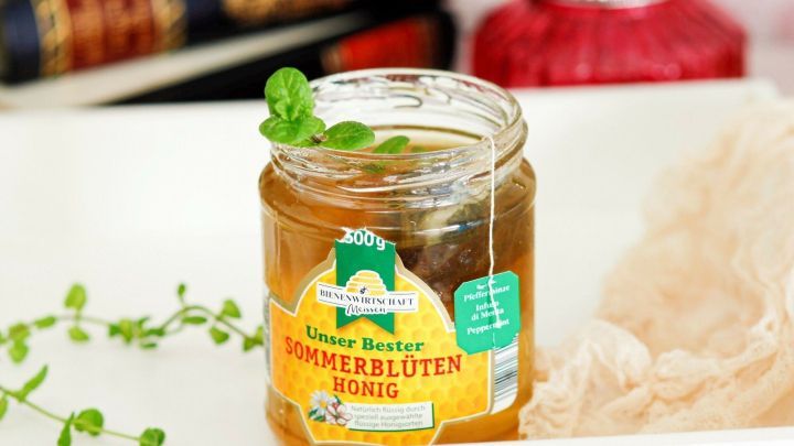 Ein Honigglas mit Sommerbl&uuml;tenhonig steht auf einem dekorativen Tablett, umgeben von frischen Minzbl&auml;ttern.