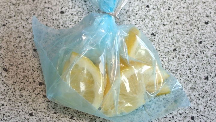 In einer blauen T&uuml;te befinden sich gefrorene Zitronenscheiben, die auf einer grauen Arbeitsplatte liegen.