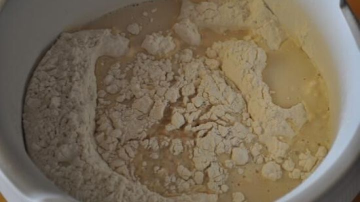 Eine Sch&uuml;ssel mit Hefeteigzutaten: Mehl, Wasser und Hefe, unvermengt in einem wei&szlig;en Beh&auml;lter auf einem K&uuml;chentisch.