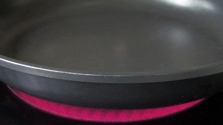 Eine Pfanne liegt auf einem Herd, w&auml;hrend die Hitze unter ihr sichtbar rot leuchtet, bereit zum Braten ohne Anbrennen.