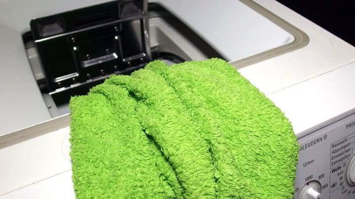 Ein leuchtend gr&uuml;nes Tuch h&auml;ngt &uuml;ber eine Waschmaschine, w&auml;hrend die T&uuml;r offen ist, bereit zum Waschen neuer Kleidung.