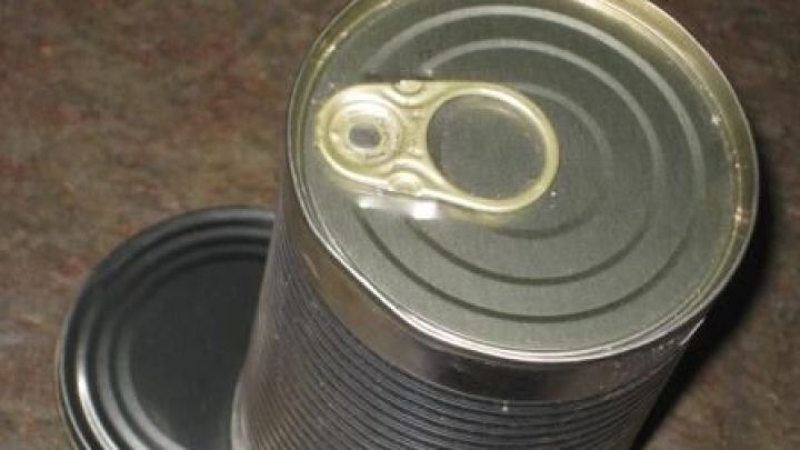 Eine ge&ouml;ffnete Konservendose steht auf einer dunklen Oberfl&auml;che, der Deckel liegt daneben.