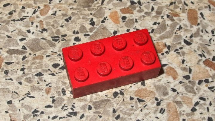 Ein roter Legostein liegt auf einer gemusterten, rauen Oberfl&auml;che und wartet darauf, gereinigt zu werden.