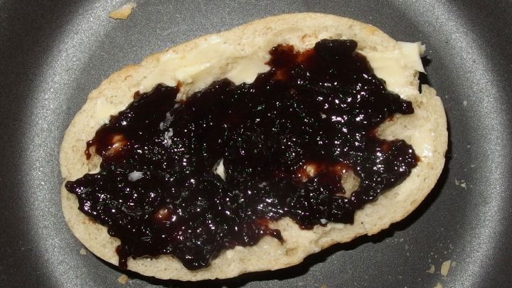 Ein belegtes Br&ouml;tchen mit dunklem Pflaumenmus liegt in einer Pfanne. Der Kontext ist eine einfache K&uuml;chensituation.