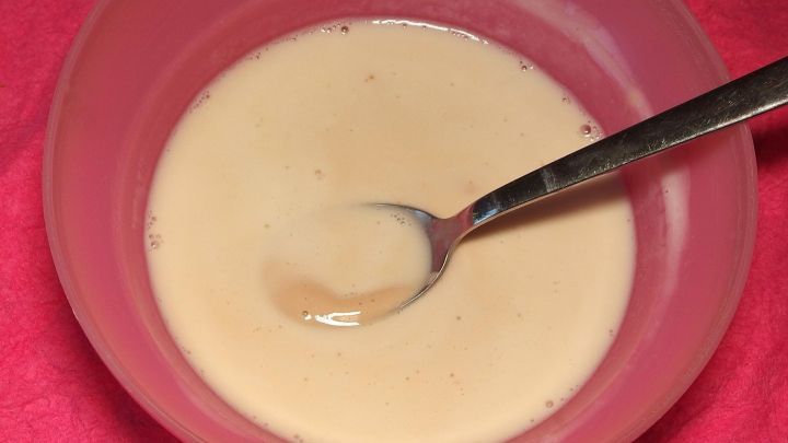 Eine cremige Gesichtsmaske aus Hefe befindet sich in einer Sch&uuml;ssel, w&auml;hrend ein L&ouml;ffel darin r&uuml;hrt. Der Hintergrund ist pink.