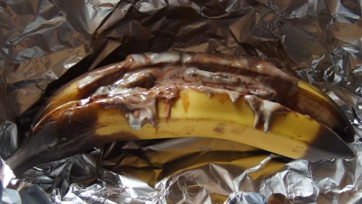 Eine Schokobanane aus dem Ofen liegt in Alufolie, w&auml;hrend die Schokolade &uuml;ber die Banane schmilzt und sich vermischt.