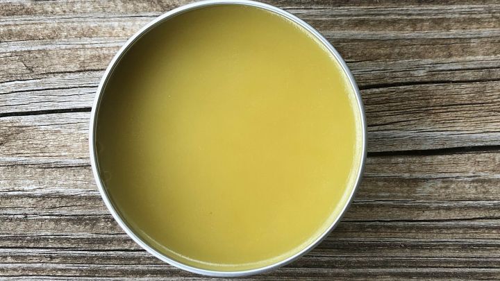 Ein rundes Beh&auml;ltnis mit gelbem Erk&auml;ltungsbalsam steht auf einer Holzoberfl&auml;che, umgeben von nat&uuml;rlicher Textur.