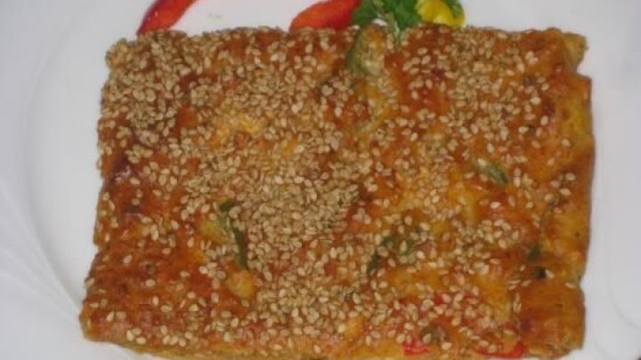 Ein quadratisches St&uuml;ck Schafsk&auml;se-Paprikakuchen liegt auf einem wei&szlig;en Teller, umgeben von frischem Gem&uuml;se.