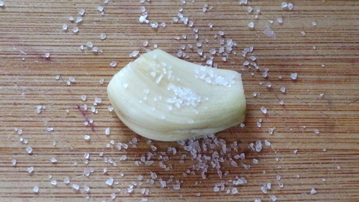 Eine Knoblauchzehe liegt auf einem Holzbrett, umgeben von grobem Salz, das das knoblaucharomatische Geschmackserlebnis intensiviert.