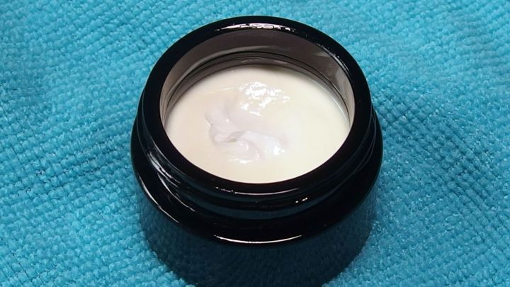 Eine schwarze, runde Dose mit einer erfrischenden Gesichtsmaske steht auf einem blauen Tuch, bereit zur Anwendung.